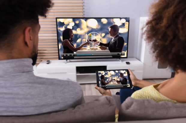 Young,Couple,Sitting,On,Sofa,Connecting,Television,Channel,Through,Wifi